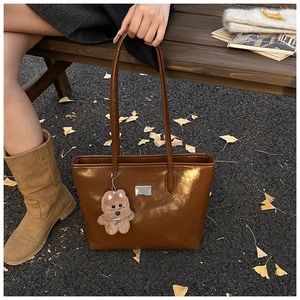 Detail of vintage brown leather underarm bag with cute teddy bear charm on autumn background