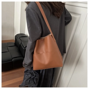 Close-up of caramel leather shoulder bag with vertical stitching on minimalist bucket design