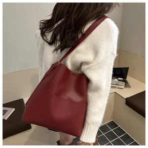 Detail view of a burgundy leather bucket bag with vertical stitching on a female model