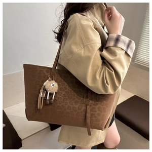 Détail d'un cabas marron foncé à motif léopard avec un charm en peluche sur un manteau