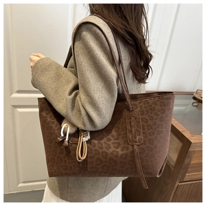 Detail of leopard print tote bag with brown leather straps and tassel on model