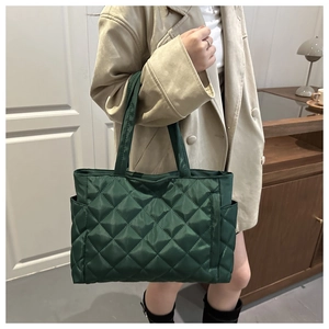 Detail of dark green quilted tote bag featuring classic diamond pattern and side pocket