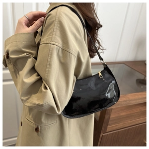 Detail of black patent leather hobo bag with gold zipper worn with khaki trench coat