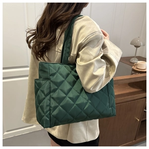 Model wearing dark green quilted nylon tote bag with rhombus pattern in soft interior lighting