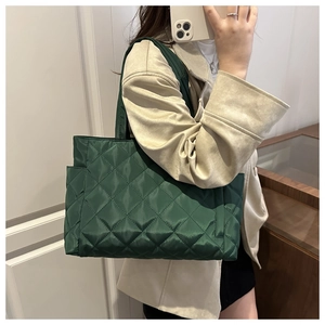 Close-up of dark green quilted tote bag showing nylon texture and side pocket detail