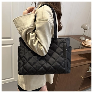 Detail of black quilted puffer tote bag with side pocket shown on shoulder