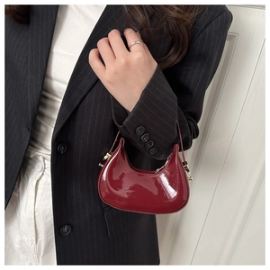 Detail of burgundy glossy patent leather crescent handbag held by model in professional suit