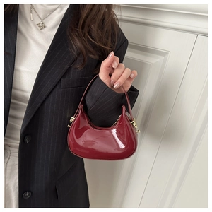 Detail of a burgundy patent leather mini half-moon bag held by a model in a striped suit