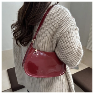 Detail view of red patent leather crescent bag on shoulder with beige knitted sweater