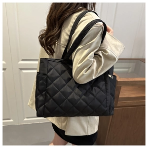 Detail of black quilted tote bag with side pocket and shoulder straps on a casual model