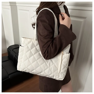 Detail of white quilted tote bag featuring a side pocket and smooth golden zipper
