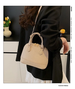 Detail of beige crocodile pattern shell bag with golden zipper and leather handle