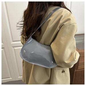Blue-grey patent leather shoulder bag with glossy finish worn by a model in a trench coat