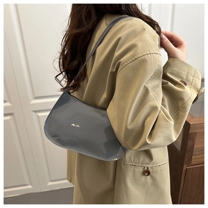 Close-up of grey patent leather shoulder bag with sleek glossy finish on a female model