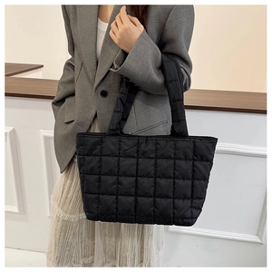 Detail of black quilted tote bag with puffer texture styled on model in grey blazer