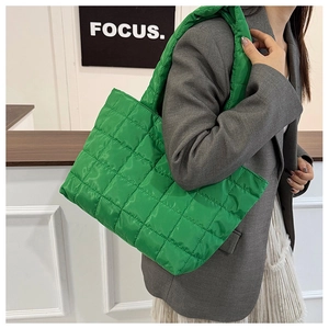 Detailed view of bright green quilted tote bag worn over the shoulder with grey suit