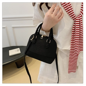 Detail of black crocodile-embossed shell bag with gold hardware and dual top handles