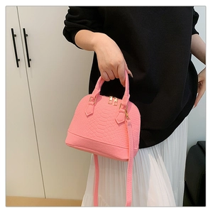 Detail of bright pink shell bag with crocodile texture, gold hardware and long strap