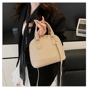 Chic beige shell bag with crocodile texture held by model in minimalist office setting