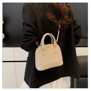 Detail of beige crocodile pattern shell bag showing dual handles and gold zipper hardware