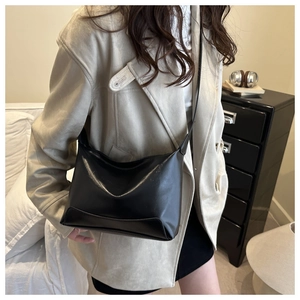 Detail of a black glossy leather tote bag shown on a model in a cozy interior setting