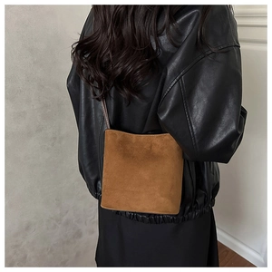 Detailed side view of a brown suede bucket bag with a slim dark brown leather strap