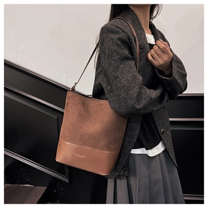 Detailed view of brown bucket shoulder bag with textured stitching on dark grey suit outfit