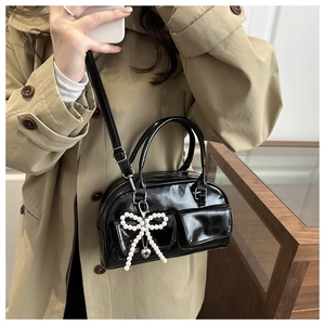 Detail of black patent leather bowling bag with pearl bow charm on khaki trench coat