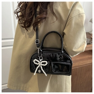 Close-up of black patent leather handbag with pearl bow pendant and heart detail