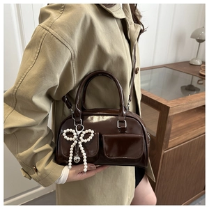 Detail of dark brown patent leather bag with silver buckles and pearl bow charm accessory