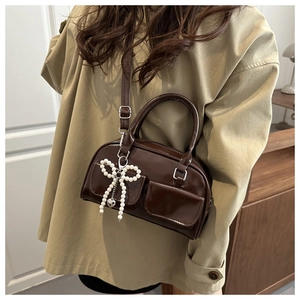 Detail of coffee brown patent leather crossbody bag with pearl bow and dual pockets