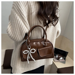 Detail view of brown underarm bag with bead bow charm on a beige knit sweater