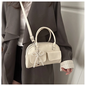 Detail of cream shoulder bag featuring beaded bow charm and dual front pockets