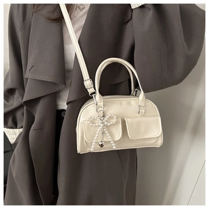 Detail of cream PU leather bowling bag with pearl bow charm and dual front flap pockets