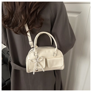 Detail of a creamy white soft leather bowling bag with pearl bow charm and heart pendant