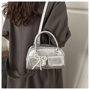 Detail of silver metallic handbag featuring two front pockets and pearl bow charm accessory