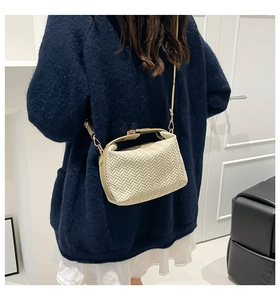 Detail of woven texture on minimalist cream crossbody bag with gold metal hooks