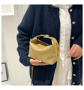 Detail of woven texture handbag with gold buckle and adjustable strap on a navy knit
