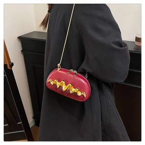 Detail of burgundy wavy metal crossbody bag with gold chain strap on black coat