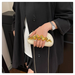 Detail of cream evening clutch bag featuring a gold wavy ring handle and chain strap