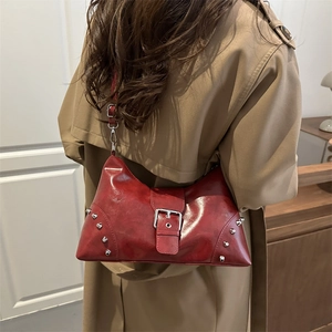 Sac à bandoulière rouge en similicuir avec boucle argentée et rivets sur un trench