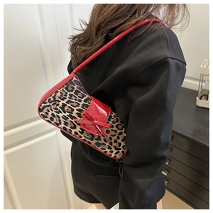 Detail of leopard print handbag featuring red patent leather bow and shoulder strap accent