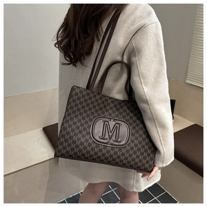 Detail of dark brown tote bag with M-pattern print and embossed logo on model back