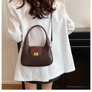 Close-up of dark brown woven crescent bag with gold buckle on a model in white blazer