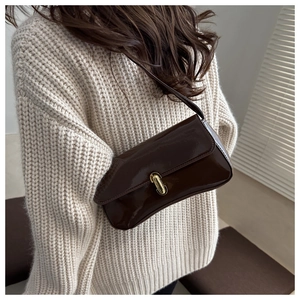 Detail of dark brown glossy underarm bag with gold metal buckle on beige sweater