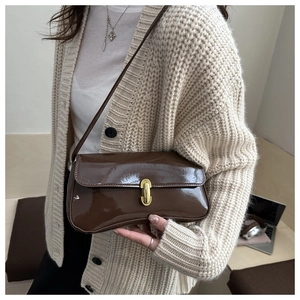 Detail of dark brown patent leather shoulder bag with gold clasp shown on a model