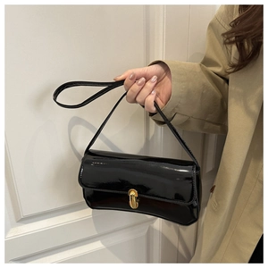 Glossy black patent leather baguette bag with a gold twist lock held by a model
