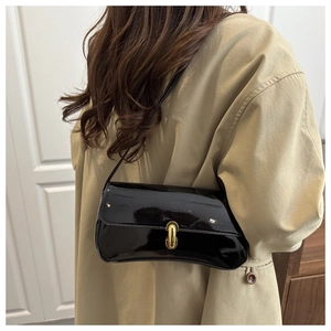 Detail view of a black glossy patent leather bag with a gold oval clasp on a beige coat