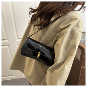 Detail of a black patent leather underarm bag with a golden twist lock on a model