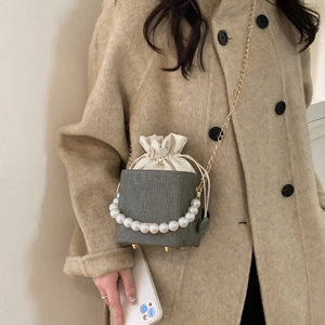 Sac seau vert foncé avec poignée en perles et chaîne dorée porté sur un manteau beige